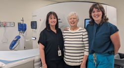 Three women stand in front of a new CT Scanner mac